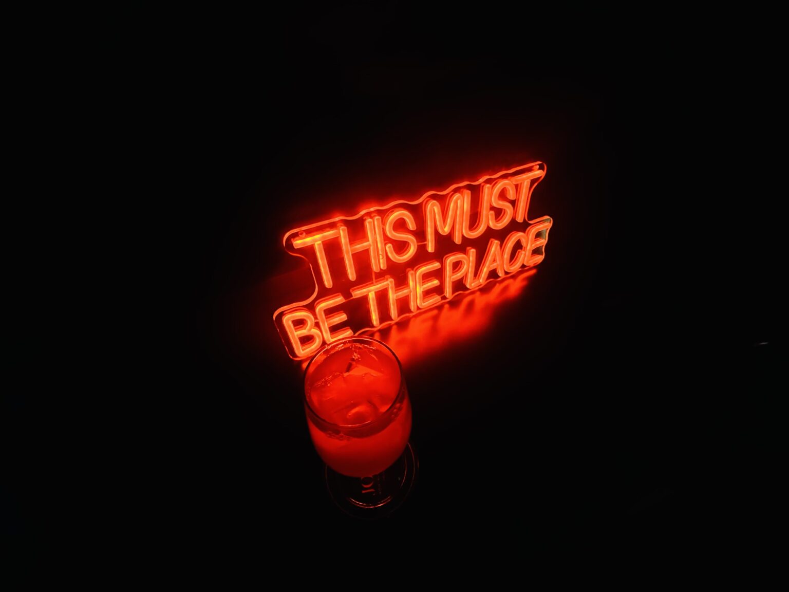 A neon sign reading This Must Be The Place above a glowing red glass
