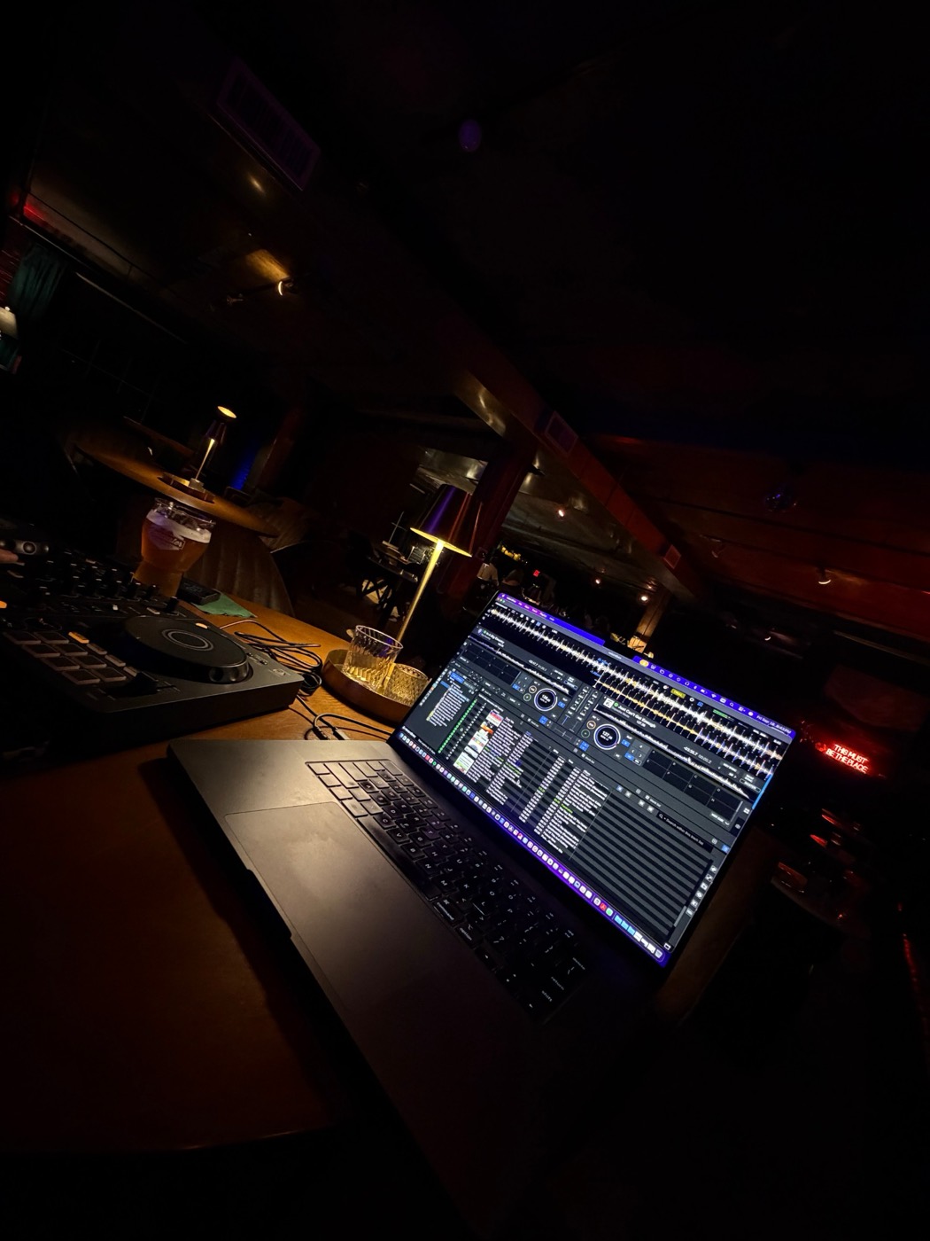 A DJ setup on a table with the This Must Be The Place neon sign glowing in the back